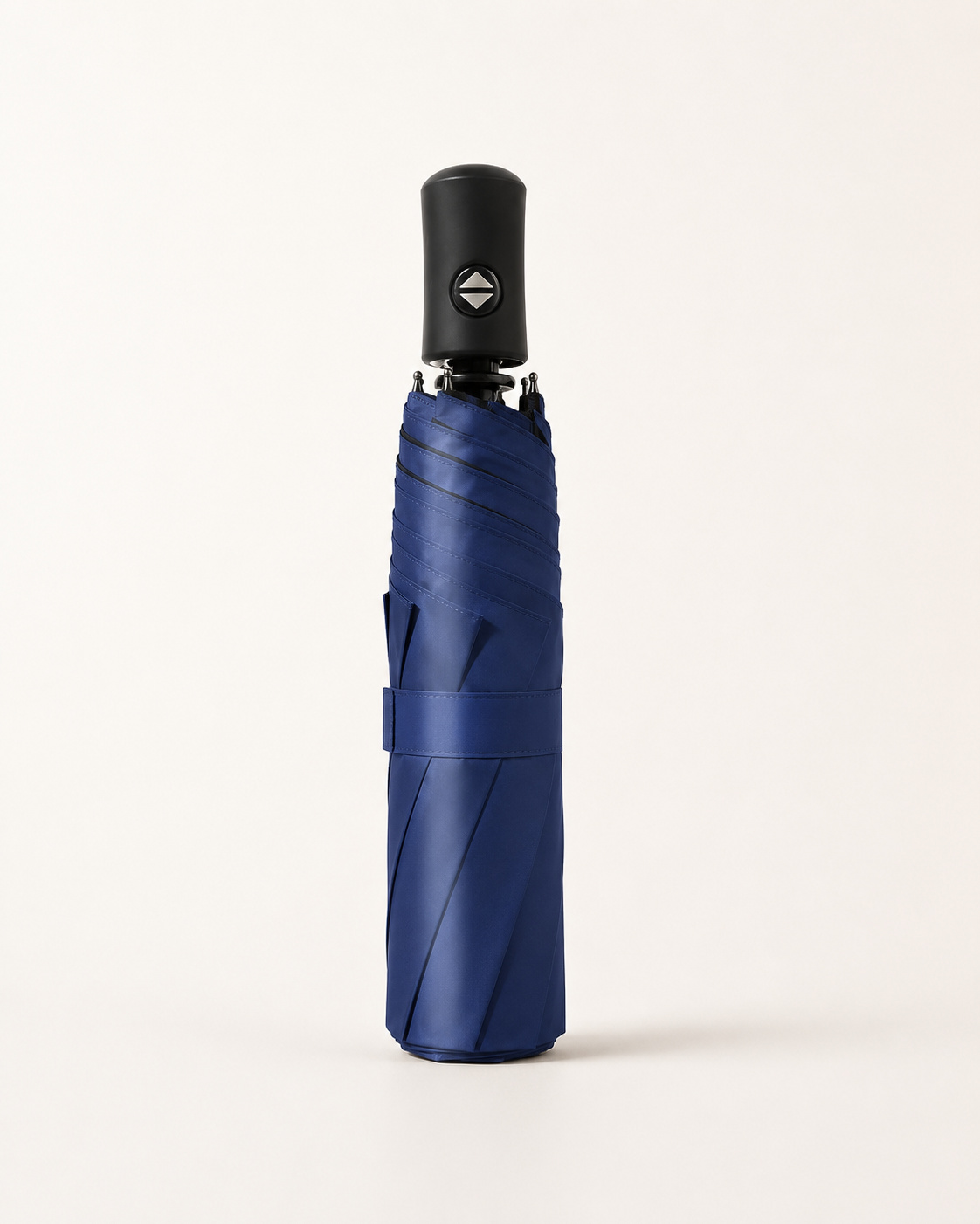 A closed, compact umbrella in a deep navy blue color, standing vertically on a clean, light beige background. It features a black handle with a small silver geometric logo.